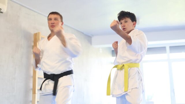 Adult man and boy teen karatekas train karate technique in studio