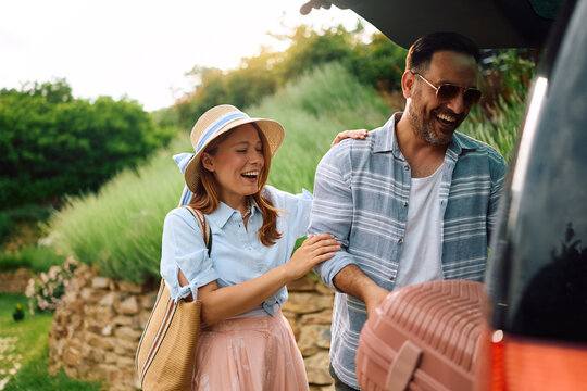 Cheerful couple loading suitcases into car trunk while going on summer vacation.