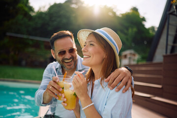 Naklejka premium Happy couple drinking cocktails relaxing by pool during summer vacation.