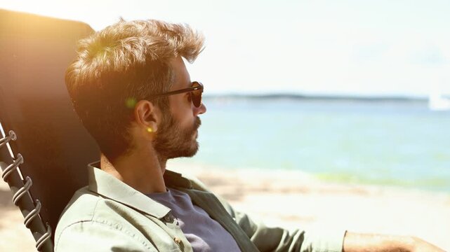 A man is sitting in a beach chair, looking out at the water