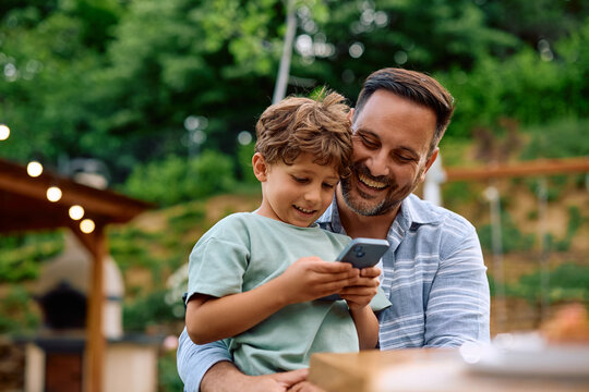 Happy father and son using smart phone while relaxing on patio.