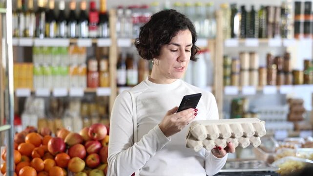 Woman store visitor buyer scan QR code on eggs label. In mobile app, client receive information about goods. Client check manufacturer data in registry database of national agency