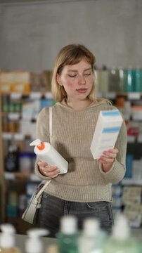 Girl in autumn clothes choosing skin cream at the drugstore. High quality 4k footage