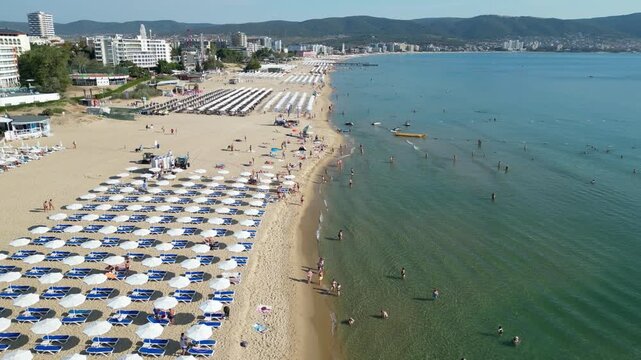 Sunny Beach coastline unfolds during a forward drone flight above the beach with rows of umbrellas and visitors along the Black Sea in Bulgaria.