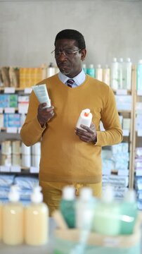 Male buyer in glasses attentively chooses skin cream at the drugstore. High quality 4k footage