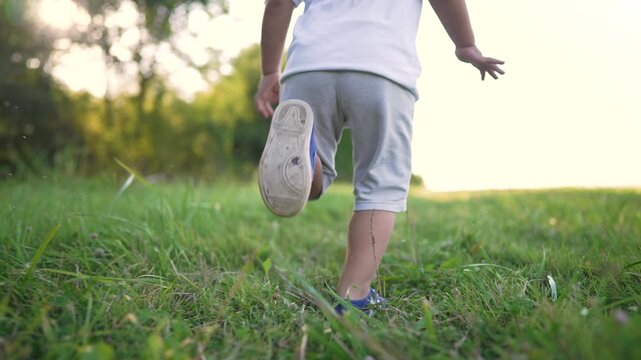 Child running through green grass field at sunset during outdoor playtime in park. Young kid enjoys active running in nature. Boy plays outdoors in summer meadow. Child moves freely in park grass.