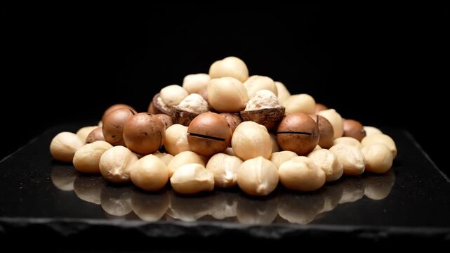Macadamia Nuts Pile on Reflective Surface with Black Background.