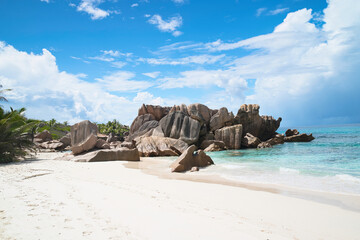 Naklejka premium Pristine tropical coastline with massive granite rocks, white sand, and turquoise water under a blue sky, Anse cocos, La Digue, Seychelles 