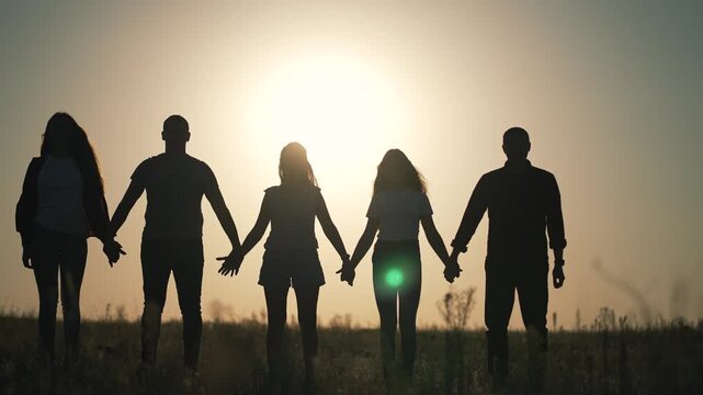 Silhouette group holding hands at sunset shows unity and teamwork. Friends unite in solidarity. People connect together in friendship. Teamwork creates strong unity bond. Group stands united together.