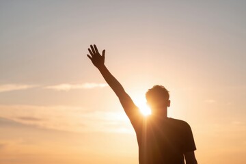 Fototapeta premium The person silhouetted against a golden sunset raising a hand toward the sky