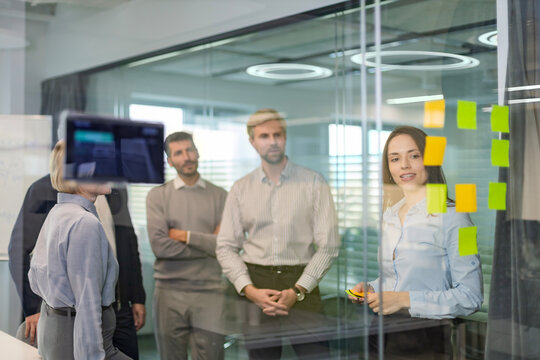 Businesspeople talking in their diverse team during a brainstorming session with sticky notes on glass wall in a modern office