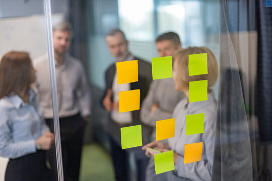 Image of business colleagues collaborating on new innovative project is blurry, sticky notes on glass wall in modern office environment