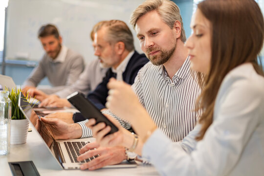 Two business people discussing work together using a smartphone in a modern office, colleagues on the background