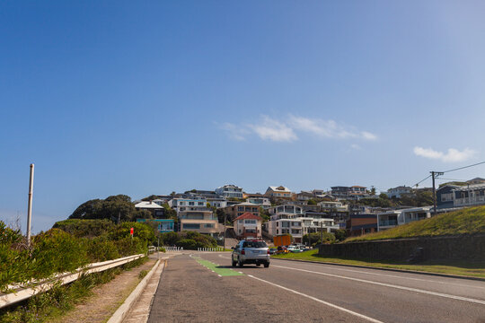 Coastal houses on hillside seen from road with car traveling through city