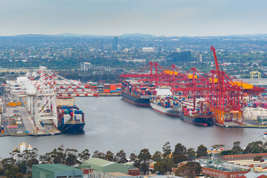 Distant aerial view of cargo ships at port under large gantry cranes