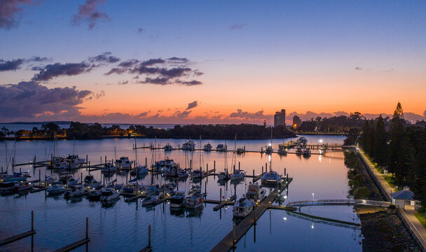 Rows of yachts and boats moored along illuminated piers at dusk