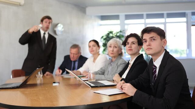 Confident interested young guy listening attentively to coach during business training in office and watching presentation