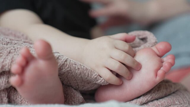 Baby hand touching adult hand wrapped in knitted blanket. Infant fingers gently holding parent palm. Newborn baby connection with mother. Tender touch between child and adult showing love.