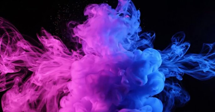 Abstract pink and blue ink clouds colliding and mixing on a black background with sparkling particles. Cinematic fluid motion of colorful smoke in slow motion.