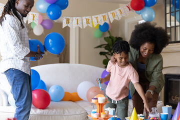 Obraz premium Family preparing birthday in living room, dad holding balloons, mom guiding child to cupcakes