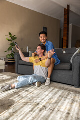 Obraz premium Male partners sitting in living room, one holding tablet leaning against gray sofa while hugging