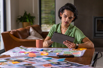 Obraz premium Asian man wearing green shirt studying at home desk holding black tablet and sticky notes