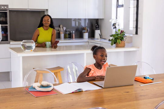 African American mother and child standing and sitting in home kitchen using laptop, headphones