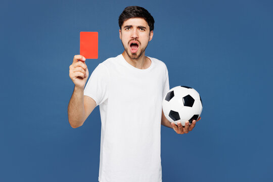 Young sad upset man fan wear white basic t-shirt cheer up support football sport team hold soccer ball red card propose player retire from field watch tv live stream isolated on plain blue background