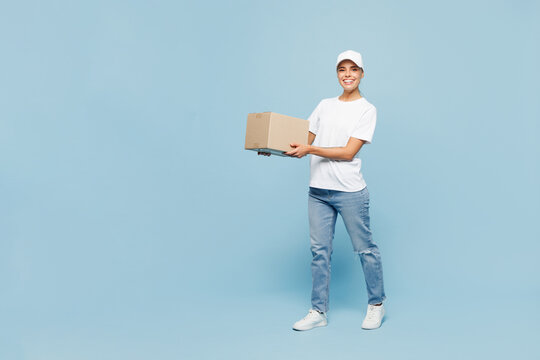 Full body delivery employee young woman wear white cap T-shirt uniform workwear work as dealer courier hold in hand cardboard box isolated on plain pastel light blue background studio Service concept