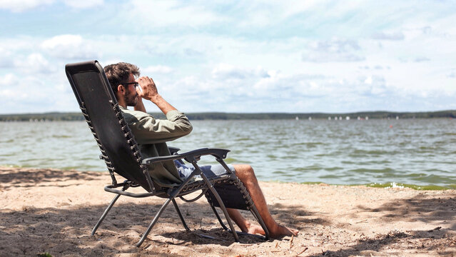 A man is sitting in a beach chair, looking out at the water