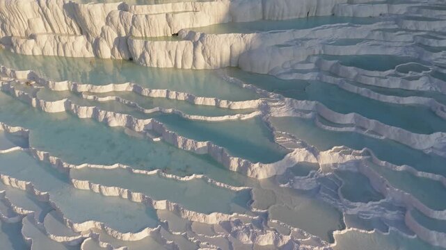 Pammukale Turkey mesmerizing travertine terraces shimmer under the soft light of dawn. Visitors walk along the mineral-rich pools and admire the natural beauty, creating unforgettable experiences.