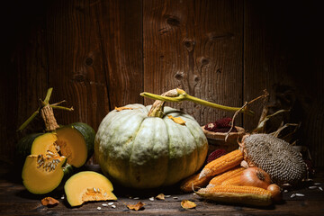 Naklejka na ściany i meble Pumpkins with cut squash, sunflower and corn cobs on wooden table against textured wall. Autumn harvest still life with Thanksgiving vegetables and warm rustic tones