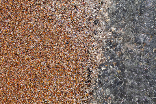 Sparkling water covering small stones and shell pieces at beach