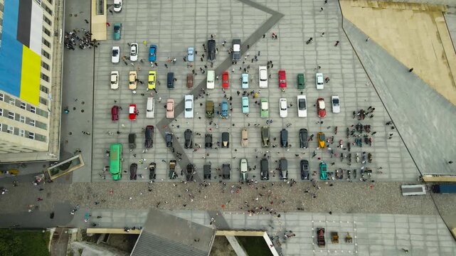 Top down aerial view of a vintage car exhibition in Freedom Square, Tallinn, Estonia, where a crowd of people is walking around and admiring the classic automobiles parked on the pavement