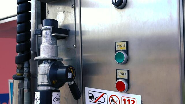 Detailed view of a CNG filling station pump with the nozzle, pressure hose, and control panel featuring start and stop buttons. The system shows ecological fuel technology for modern vehicles