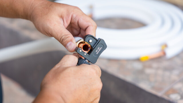 Air conditioning maintenance service using professional tube cutter tool, Close up of repairman hand cutting copper pipe for hvac system, Technician using pipe cutter for air conditioner installation