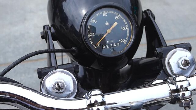 Detailed close up view of a vintage motorcycle speedometer and its chrome handlebars, capturing the classic design and instrumentation of a retro motorbike during an exhibition