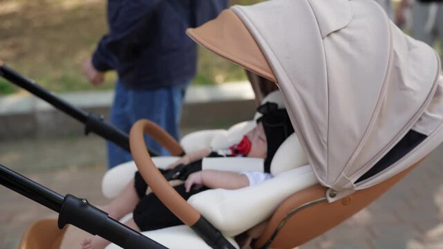 Soft canopy shields sleeping baby. Calm infant rests in gentle rocking chair. Wooden handle, padded seat, soft fabric. Parent walks nearby, out of focus. Peaceful, quiet moment for baby's nap