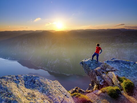 Woman standing on a rocky outcrop at Kjerag above the Lysefjord, sunset, Lyseboten, Rogaland, Norway