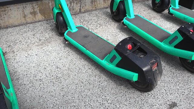 Numerous green electric scooters parked in a row on a concrete sidewalk, available for rent. Urban e mobility solutions offering an alternative and eco friendly mode of transportation in the city