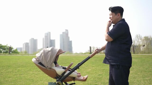 Man walks with stroller in open park space. City skyline visible behind green field. He appears relaxed, possibly thinking or resting. Ideal for family, parenting, or urban outdoor scenes
