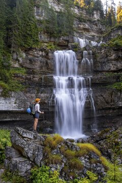 Young pretty hiker standing on rocks in front of Cascata di Mezzo waterfall, long exposure, Vallesinella, Brenta, Trentino, Italy