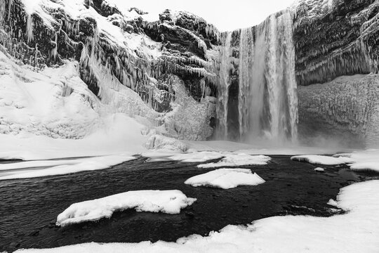 Skogafoss waterfall with icy and snowy rock face, black and white photo, Sudurland, Iceland