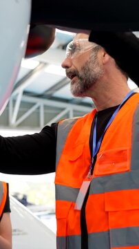 Mature aircraft mechanic inspecting airplane engine with trainee