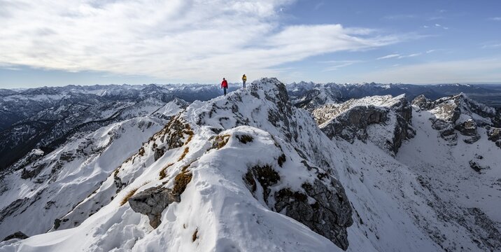 Two mountaineers on a narrow rocky snowy ridge, behind peak crow, view of mountain panorama, hiking to Ammergauer Hochplatte, in autumn, Ammergau Alps, Bavaria, Germany