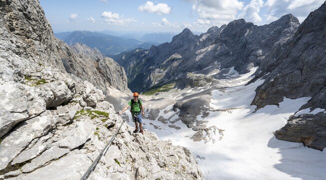 Mountaineer with helmet in a secured via ferrata, Zugspitze via ferrata, ascent to the Zugspitze, view of mountain basin with snow field of the H&ouml;llentalferner and H&ouml;llental, Wetterstein range, Bavaria, Germany