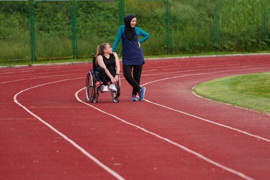 Female Wheelchair Athlete And Friend In Hijab Conversing On Outdoor Running Track