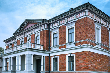 Fototapeta premium Historical red brick mansion building facade with neo-Renaissance details, columns and a balcony. Elegant European estate or historic museum exterior on a bright summer day.