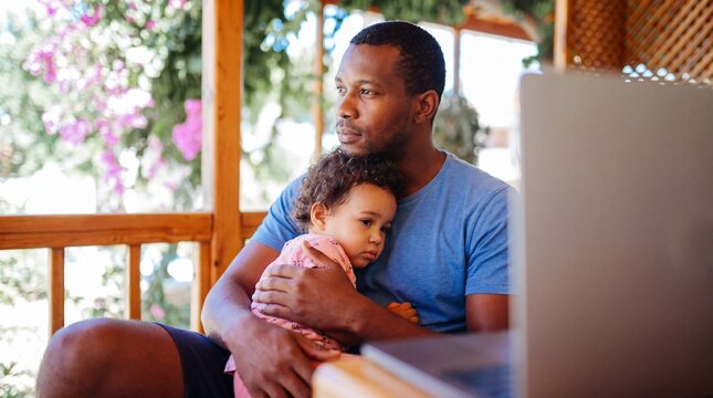 Father holds child while looking at laptop outdoors