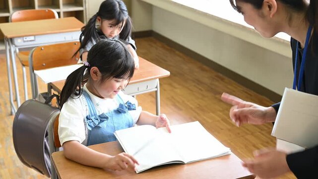 教室で女性教師の個別指導を受けて笑顔でノートを見つめる女子小学生